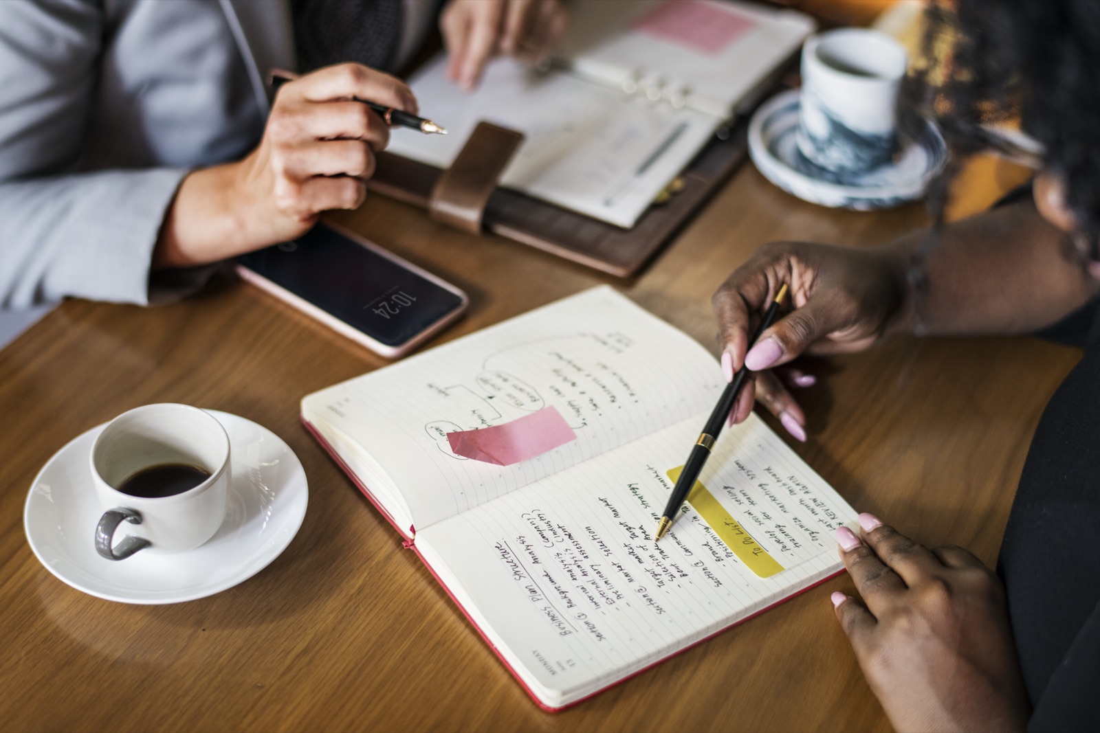 Duas profissionais de marca planejando uma campanha de UGC com caderno e celular sobre a mesa de um café.