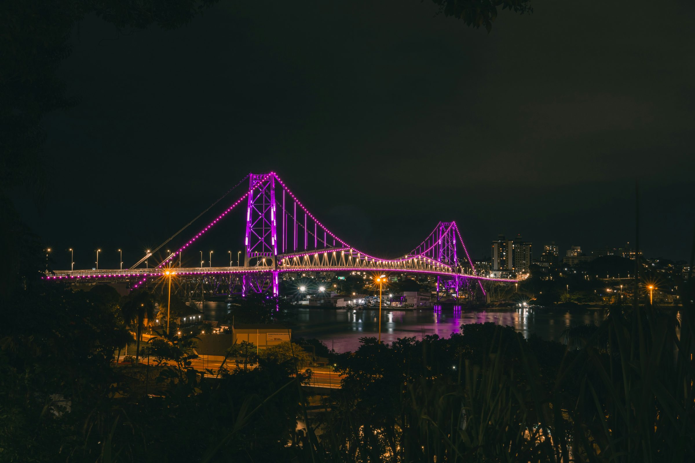 Ponte Hercílio Luz iluminada em tons de roxo à noite, em Florianópolis.