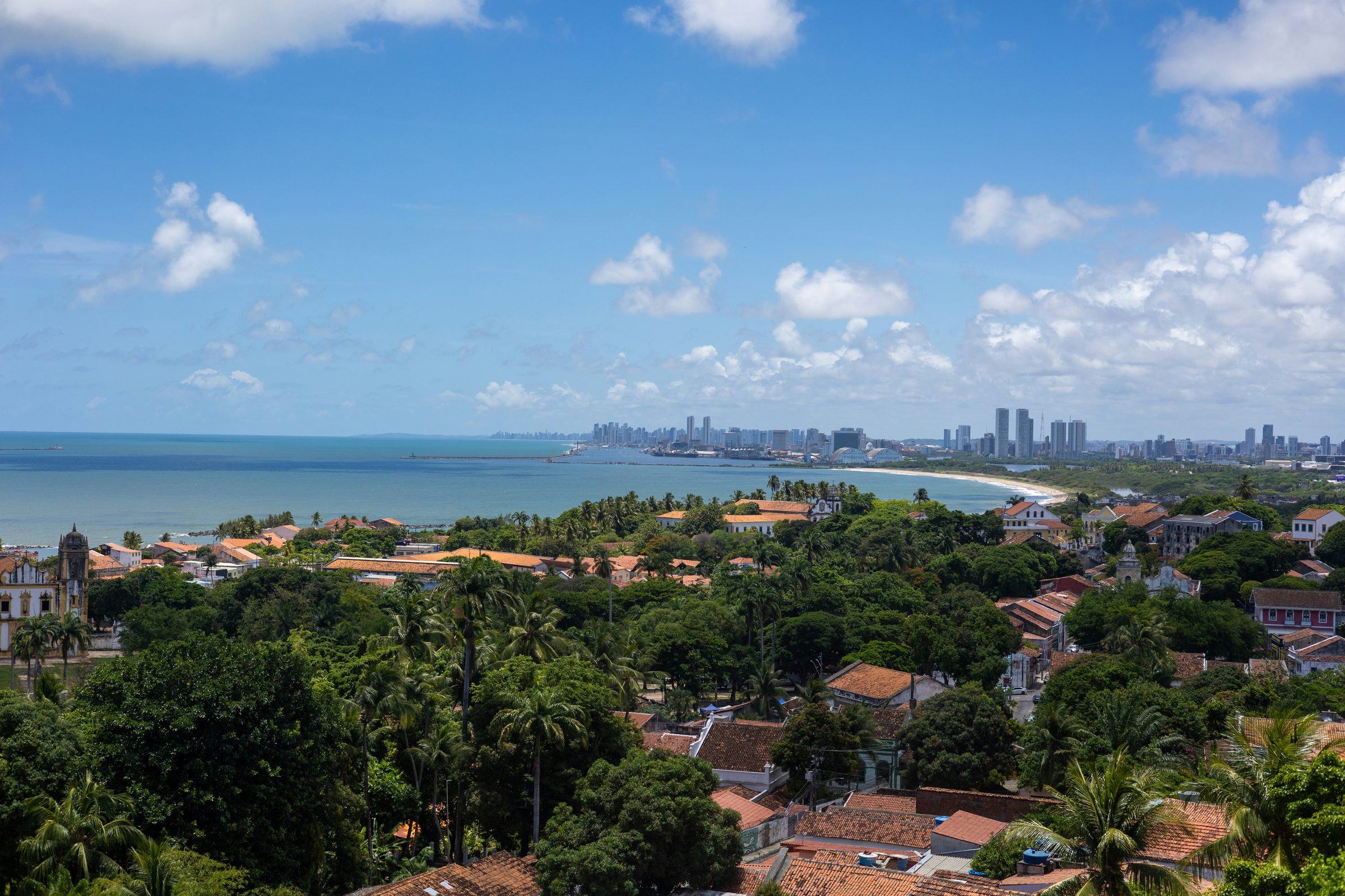 Telhados históricos de Olinda com a paisagem urbana de Recife ao fundo.